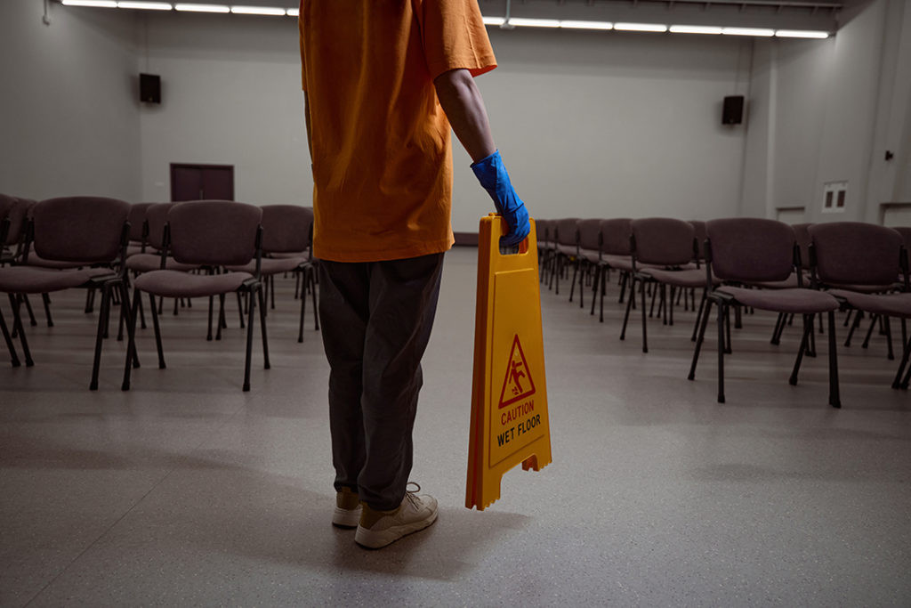 mindful janitor putting a yellow warning sign on the wet floor