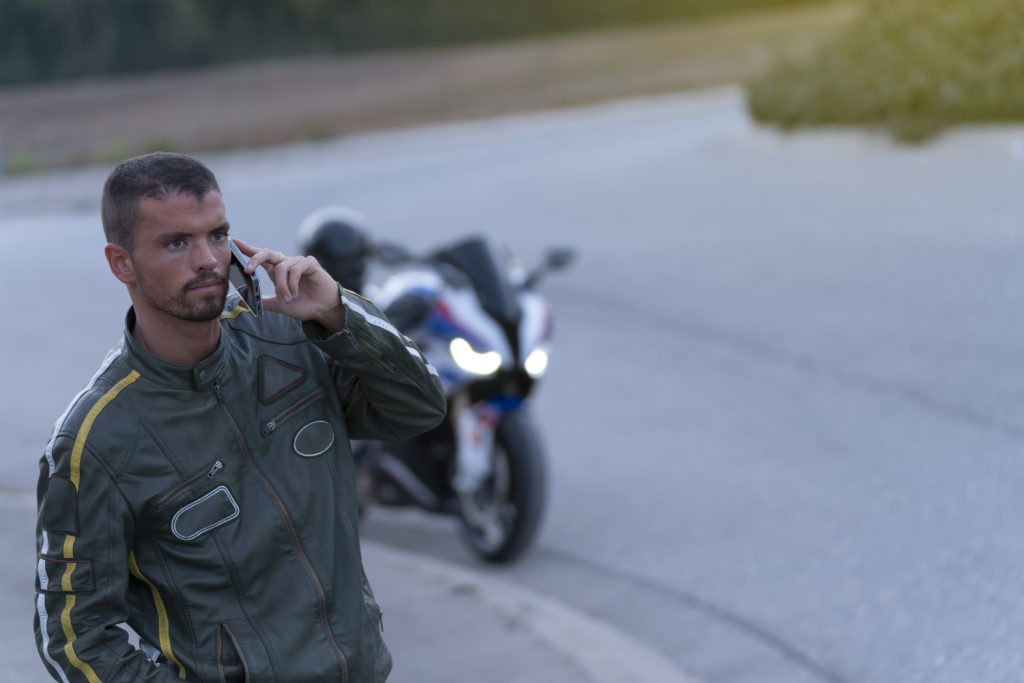 young man with motorcycle breakdown on the road talking on the phone